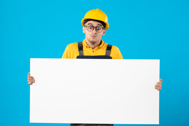 视图身着制服的男建筑工人正面图 蓝色墙上有平面图工作纸蓝色