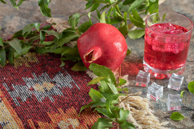 成熟冰镇果汁和石榴叶和地毯上的石头表面红色立方体玻璃