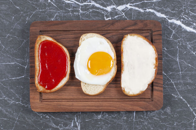 烘焙食品把鸡蛋 果酱和奶酪分别放在木板上的面包片上 放在大理石表面烘焙面包切片