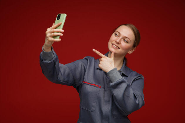 自拍微笑的年轻金发女工程师穿着制服指着手机自拍金发博尔多工程师