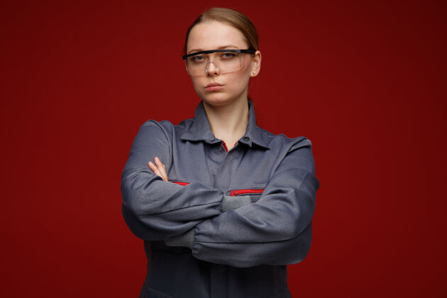 安全自信的年轻金发女工程师穿着制服 戴着安全眼镜 站着 姿势紧闭戴工程师年轻