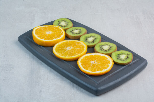 有机橘子和猕猴桃片放在深色盘子里水果柑橘成熟