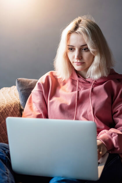 多媒体年轻的内容创造者金发女孩坐在沙发上的笔记本电脑上在家工作工作彩色远程