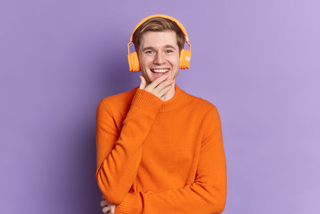 歌曲帅哥笑容可掬表达积极情绪戴着橙色套头衫通过立体声耳机收听音轨立体声娱乐科技