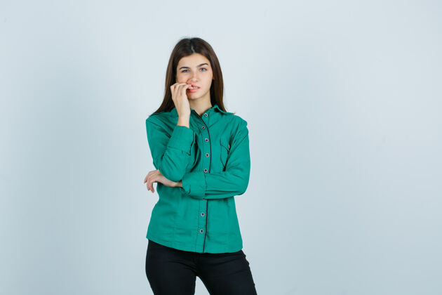 衬衫年轻的女性咬指甲在绿色的衬衫 裤子和看起来麻烦前视图咬前面房间