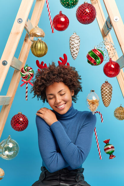 魔术开心的非裔美国女人在家享受节日的神奇气氛穿着舒适的高领毛衣摆姿势牙齿坐着垂直