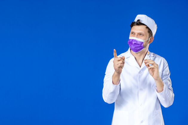 药品身穿医疗服 戴着紫色口罩的男医生正对着蓝色的脸拿着针剂医院治疗男医生