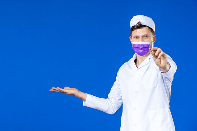 药品身穿医疗服 戴着紫色口罩的男医生正对着蓝色的脸拿着针剂病毒医院治疗