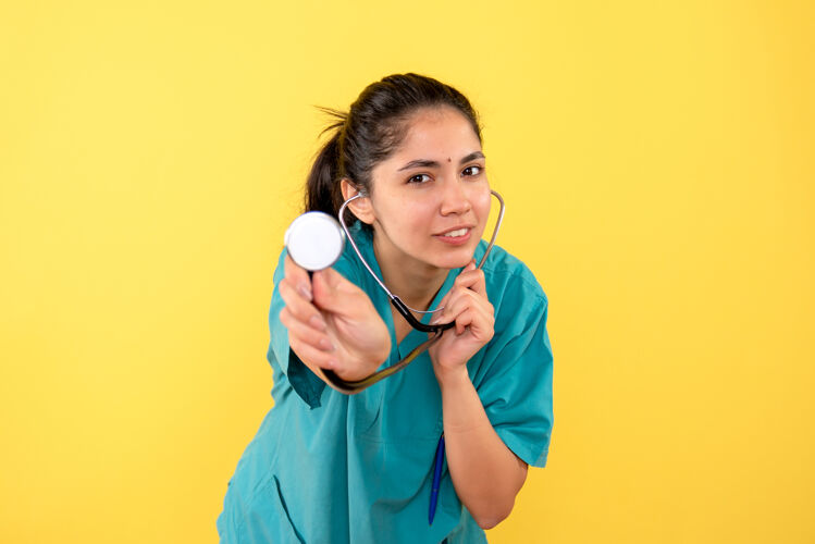 护士正面图：身着制服的幸福女医生在黄色背景上展示听诊器成人正面专业