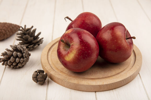 木材俯瞰美味的红苹果在一个木制厨房板与松果隔离在一个白色的木制表面中心水果木板