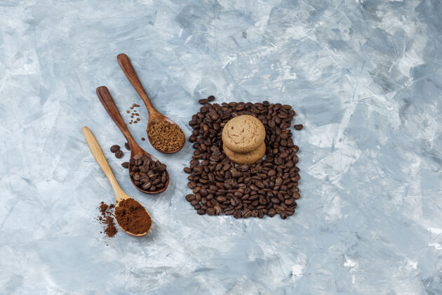 早餐一套咖啡豆 速溶咖啡 咖啡粉在木制勺子和饼干上的浅蓝色大理石背景高角度视图意式浓缩咖啡大理石木头