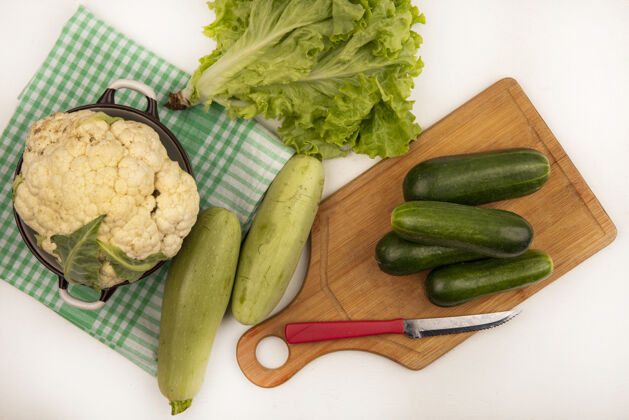 板绿色格子布上碗上的白色大花椰菜俯视图 木制菜板上放着黄瓜 菜刀将西葫芦和莴苣隔离在白色表面厨房新鲜配料
