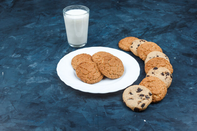 脆高角度观看花生酱饼干在白色盘子与牛奶 不同类型的饼干在深蓝色背景水平黄油薯片食物
