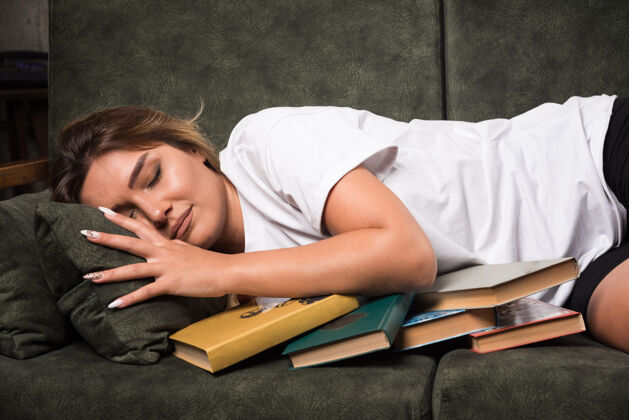 放松年轻的女人躺在沙发上 满满的书室内年轻公寓