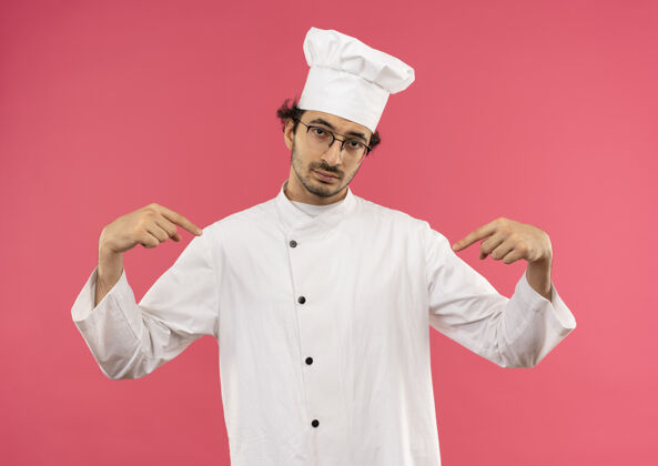 烹饪自信的年轻男厨师穿着厨师制服 戴着眼镜指着自己穿眼镜自己