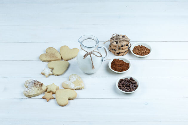 豆子一些不同类型的饼干与咖啡豆 速溶咖啡 可可 牛奶壶在白色木板背景 高角度看堆处理小吃