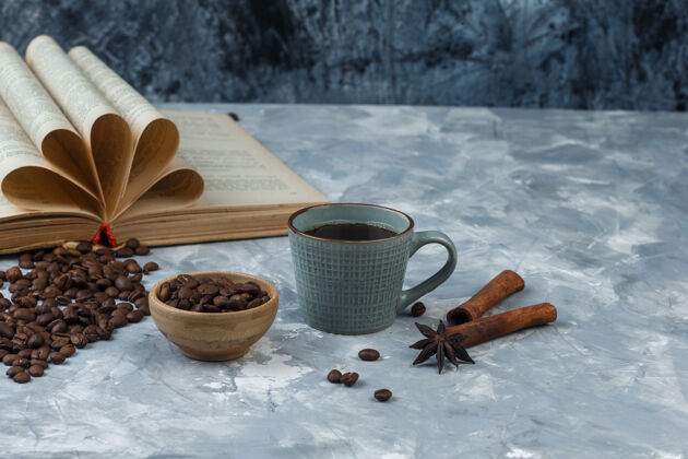 豆子咖啡豆在一个木制的碗里与书 肉桂 一杯咖啡高角度的观点对一个光明和深蓝色大理石背景肉桂笑声想法