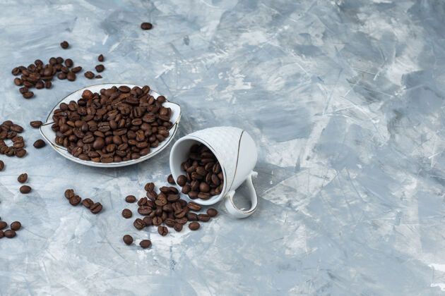 角咖啡豆在白色杯子和盘子上 灰色灰泥背景高角度视图农作物豆类种子