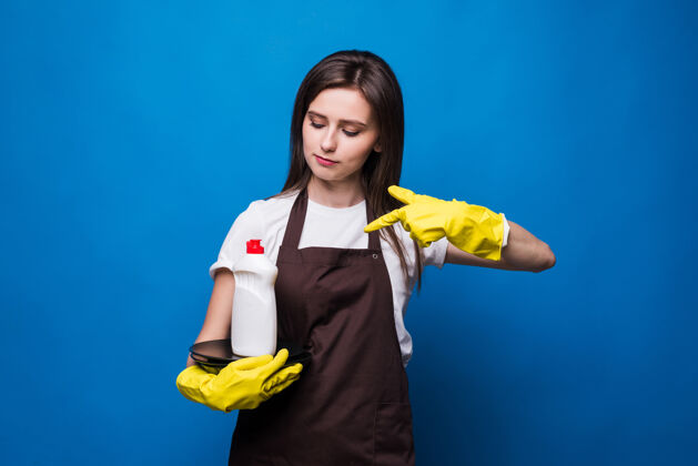 女人穿着围裙的年轻漂亮女人 手里拿着洗过的盘子和香皂一瓶香皂 在一叠干净的盘子上贴着空白标签洗碗机软肥皂