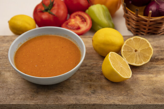 板木制菜板上碗里美味的小扁豆汤的俯视图 桶上放着柠檬和红洋葱 西红柿和辣椒被隔离在白色的表面上菜肴汤洋葱