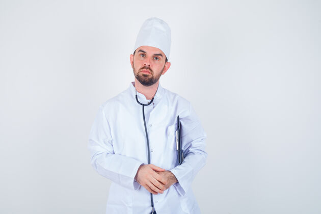 肖像年轻的男医生拿着剪贴板 穿着白色制服 表情严肃 正对着镜头沉思医院屏幕