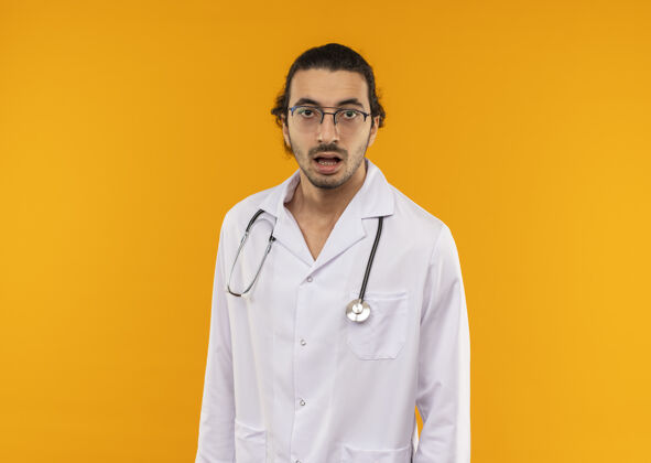 惊喜惊讶的年轻医生戴着医用眼镜 穿着带听诊器的医用长袍医疗长袍医生