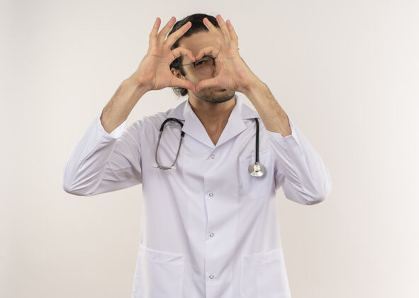 男人年轻的男医生戴着眼镜 穿着白色长袍 听诊器显示心脏的姿势手势表演医生