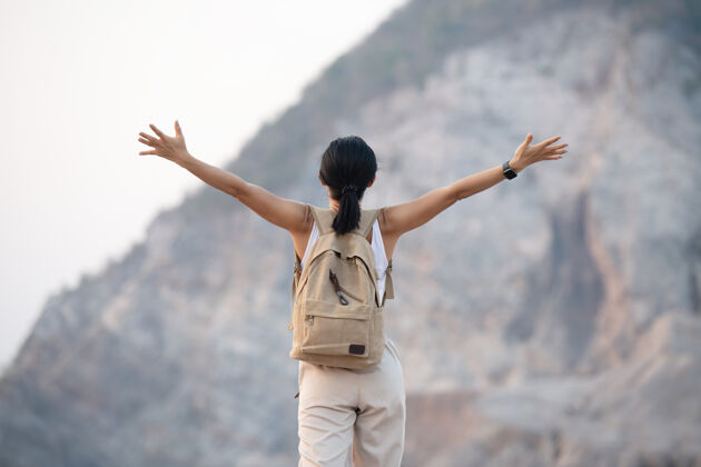 步行徒步旅行时 一位妇女在山顶举手 站在岩石山脊上的电线杆眺望着山谷和山峰乡村徒步旅行冒险