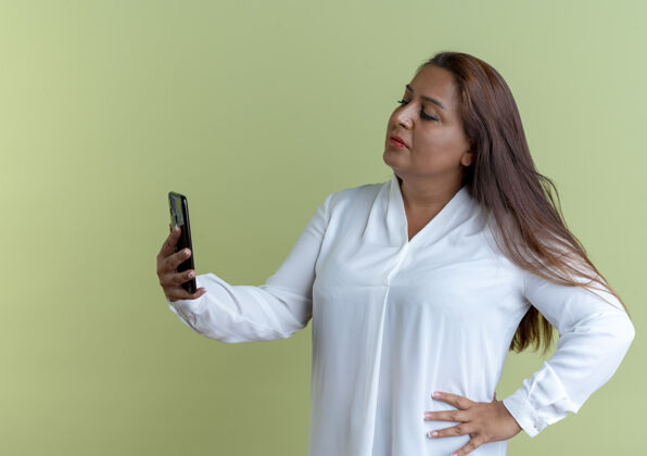 手持随意的白人中年妇女拿着手机 看着手机 把手放在臀部橄榄色休闲臀部