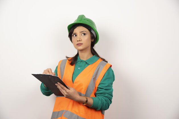 成人体贴的女工业工程师 穿着制服 白色背景上有剪贴板头盔制服安全帽