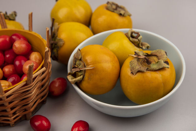 碗新鲜柿子水果的顶视图 在一个灰色的表面上 一个碗里放着一个桶里的山茱萸水果柿子秋季营养