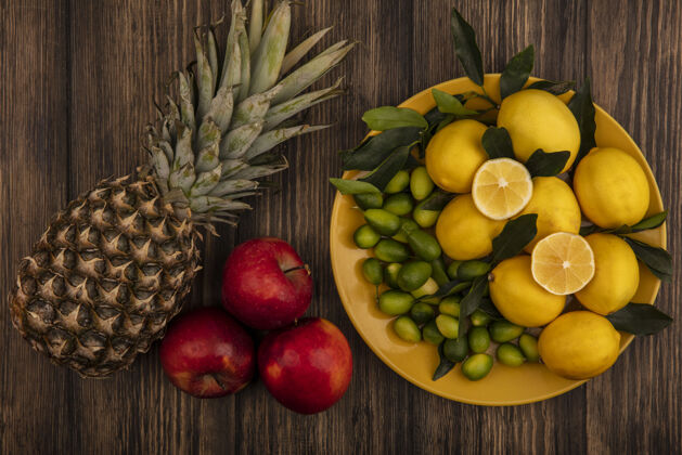 美味黄色盘子上的新鲜水果如柠檬和金盏花的俯视图 菠萝和红苹果被隔离在木制表面上配料水果素食
