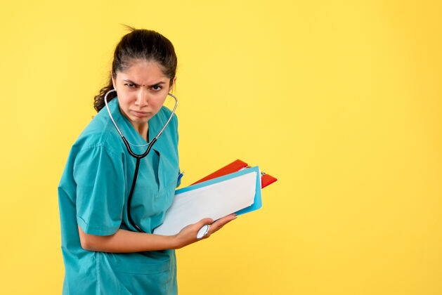 人前视图困惑的女医生穿着制服站在黄色背景上的文件纸张微笑护士