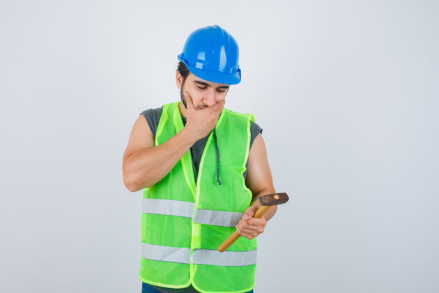 制服年轻的建筑工人穿着工装 手里拿着锤子 手放在嘴边 神情若有所思 俯瞰前方自信人肖像