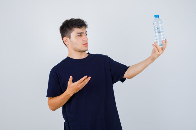 年轻一个年轻人展示着一瓶水 穿着黑色t恤 看上去很困惑正视图问题决定胡子