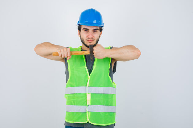 人年轻的建筑工人手持锤子 穿着工作服 握紧拳头 看上去很自信正视图英俊工作服酷