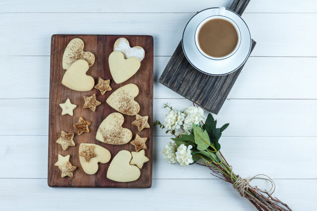 烘焙将心形和星形饼干平放在木砧板上 配上一杯咖啡 花放在白色木板背景上水平木头饼干汽水