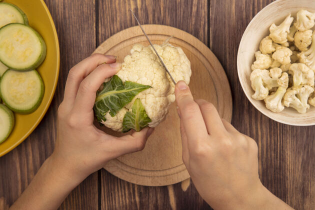 蔬菜俯视图中的女性手切菜花在一个木制的菜板与菜花芽刀在一个碗在木制表面生的饮食刀