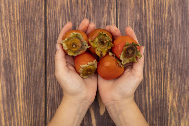 水果女性手拿着新鲜柔软多汁的柿子放在木头表面的俯视图柿子持有甜点