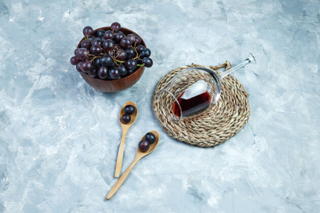 碗平放黑葡萄在碗里 木勺里放一杯葡萄酒 垫子放在灰色石膏背景上水平食物水果浆果