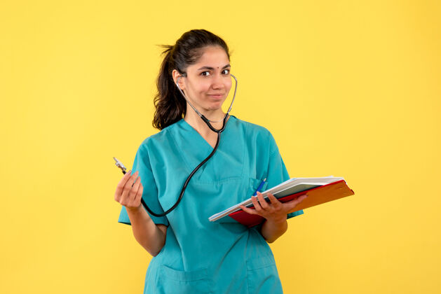 医学前视图微笑的女医生 手持听诊器站在黄色背景上听诊器从业者专业