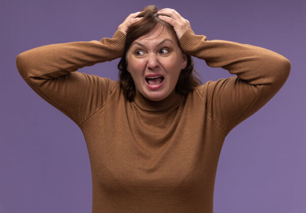 高领毛衣一个穿着棕色高领毛衣的中年妇女站在紫色的墙上狂吼着拉着头发女人站中间