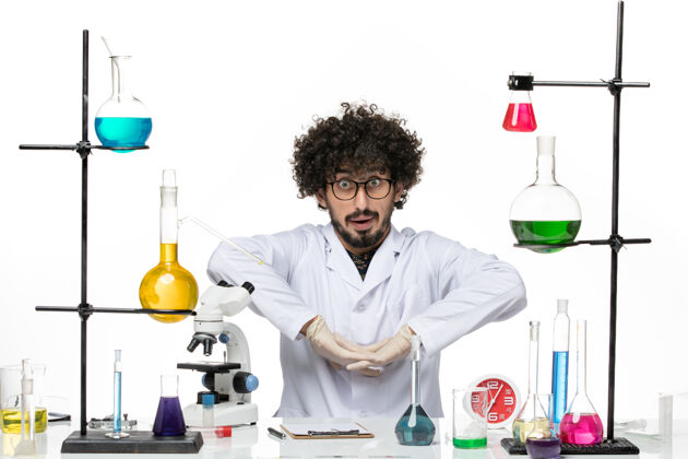 病毒正面图身着医疗服的男性化学家正坐在桌子前 白色桌子上摆着溶液套装坐着医生