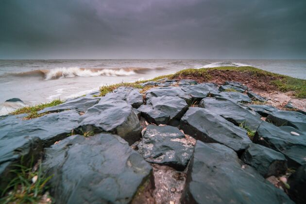 水岩石被苔藓覆盖 在傍晚多云的天空下被波涛汹涌的大海包围夜晚海洋海洋