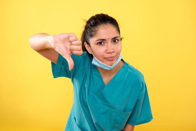 年轻女性黄色隔离墙上戴着医用面罩的年轻女性的正视图下医学人
