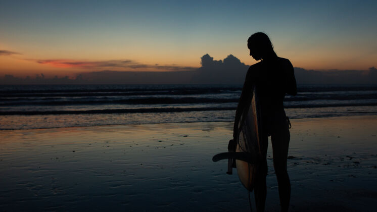 水下美丽的女孩在日落时拿着冲浪板海洋海洋女士