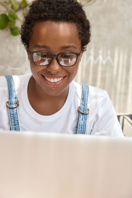 学生积极微笑的黑皮肤女友用笔记本电脑远距离工作学习满意穿孔
