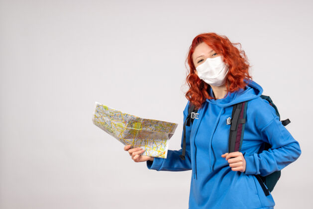 背包前视图的年轻女性与背包和地图在面具上的白墙人年轻女性地图