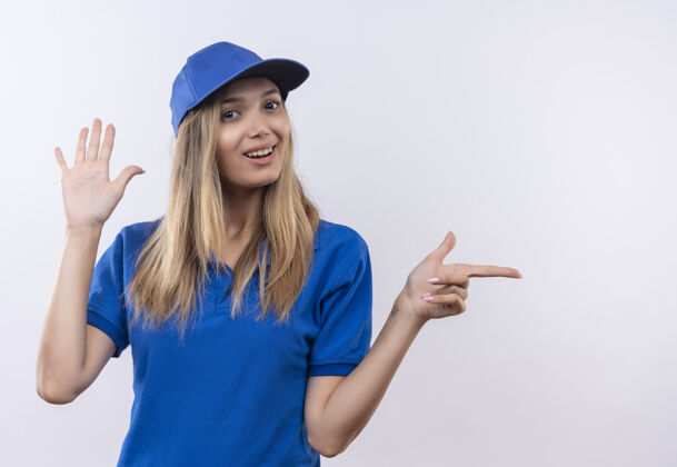 穿微笑的年轻送货女孩身穿蓝色制服 头戴帽子 显示停止的姿态 并指向隔离在白色墙上的复制空间的一边交货帽子制服
