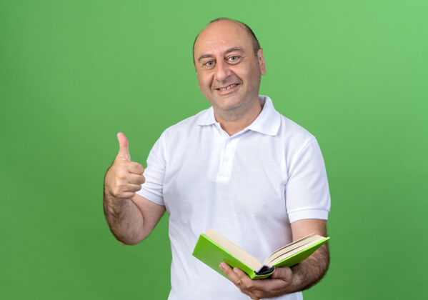 微笑微笑随意的成熟男子拿着书他的大拇指孤立在绿色的墙上成熟抱着拇指
